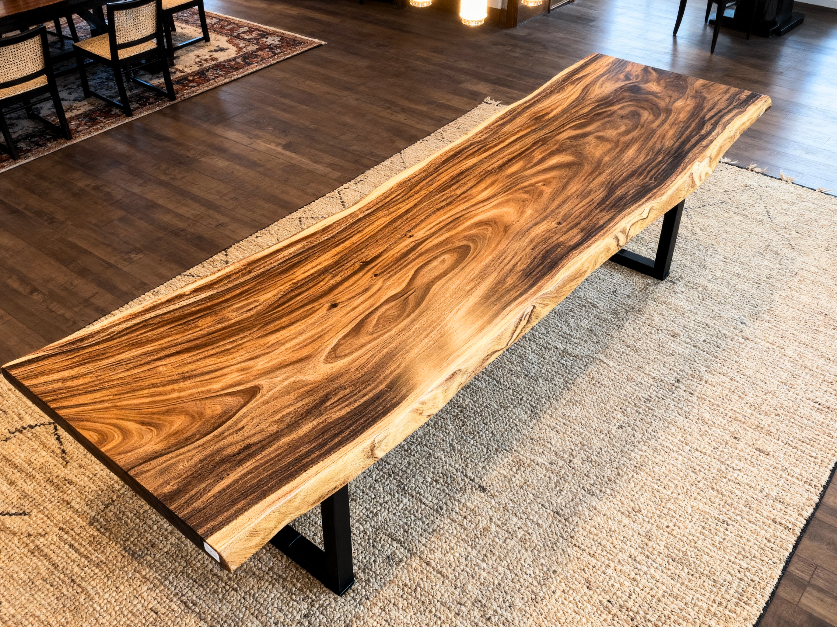 Wooden dining table with a live-edge design in a room with wooden flooring and chairs.