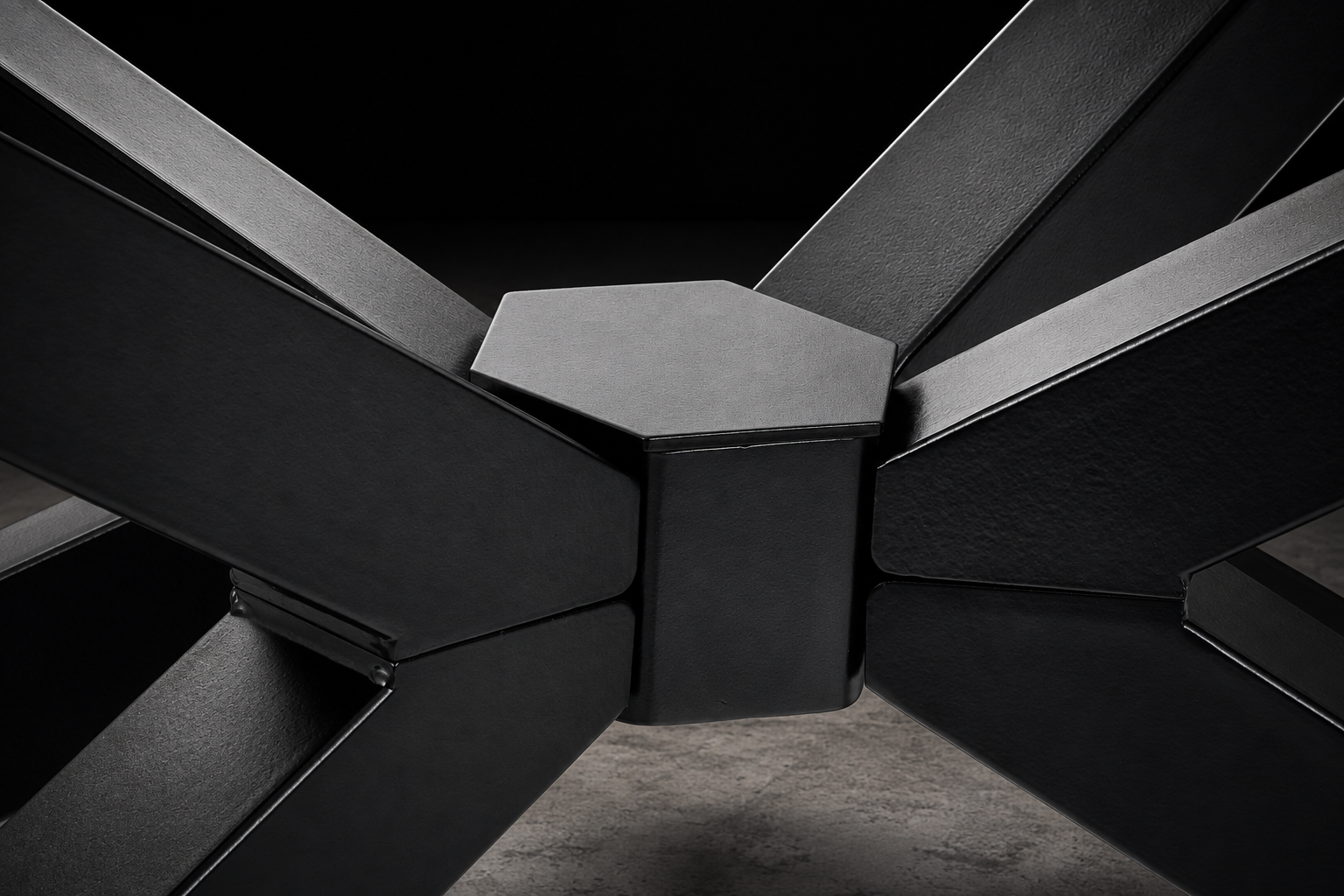 A close-up studio shot of a modern black geometric table base with angular arms radiating from a central hexagonal joint, set against a dark background.